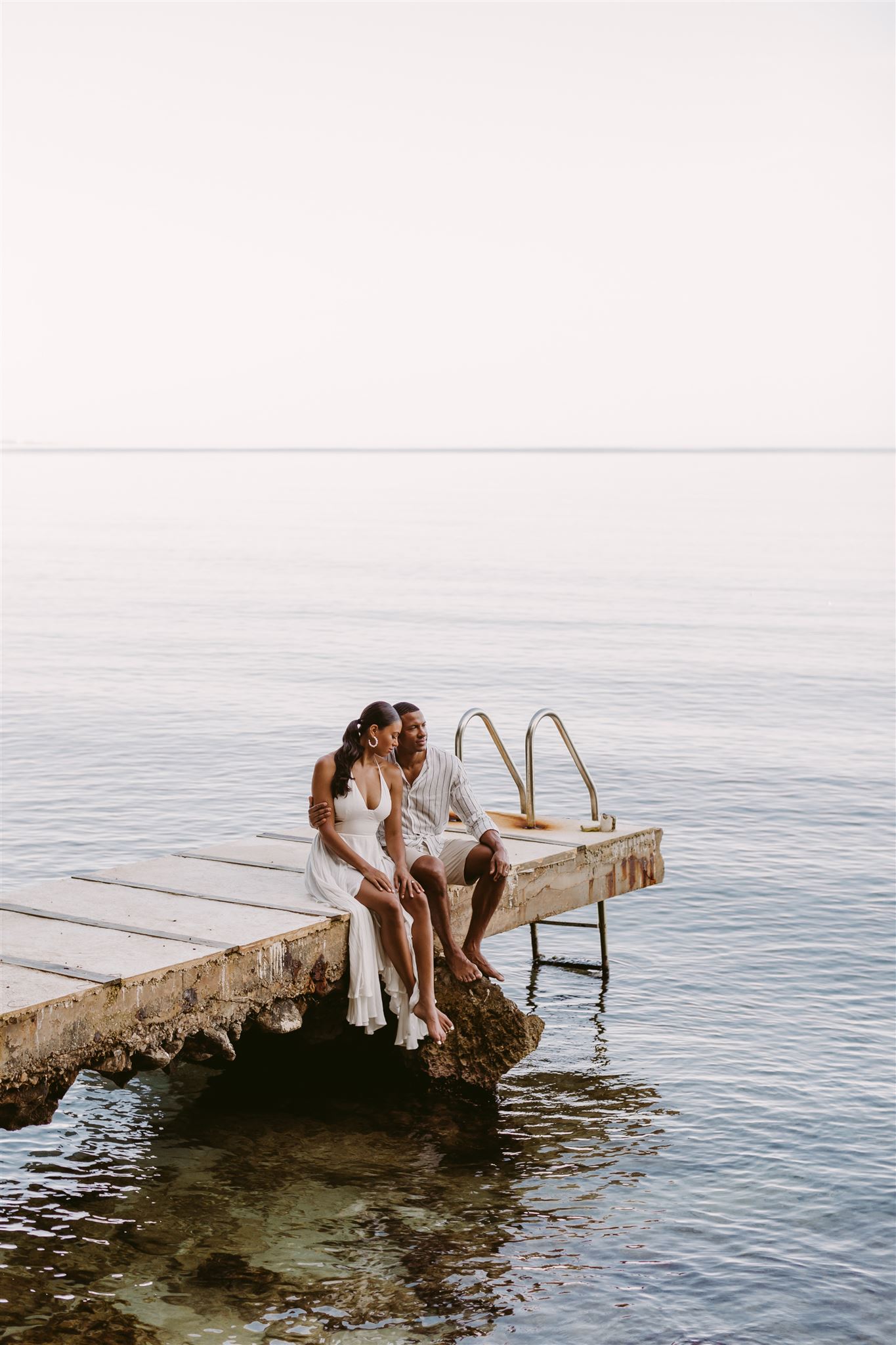 Husband Errol Barnett sits on a dock with wife Ariana Tolbert in Jamaica during their post-wedding photoshoot by Virginia luxury wedding photographer Victoria Heer.