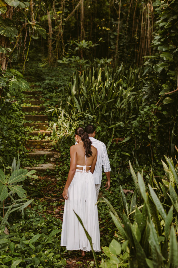 Husband and wife Errol Barnett and Ariana Tolbert hold hands as they venture into the tropical woods in Jamaica during their post-wedding photoshoot by Virginia fine art wedding photographer Victoria Heer.