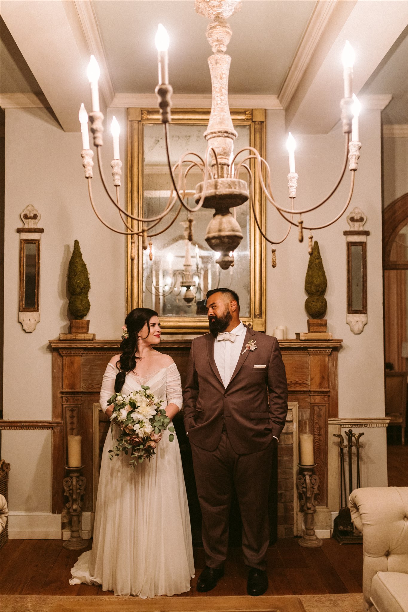 Bride and groom stand next to eachother and smile in front of the fireplace at the Retreat at Cool Spring. Image by Victoria Heer, fine art wedding photographer.