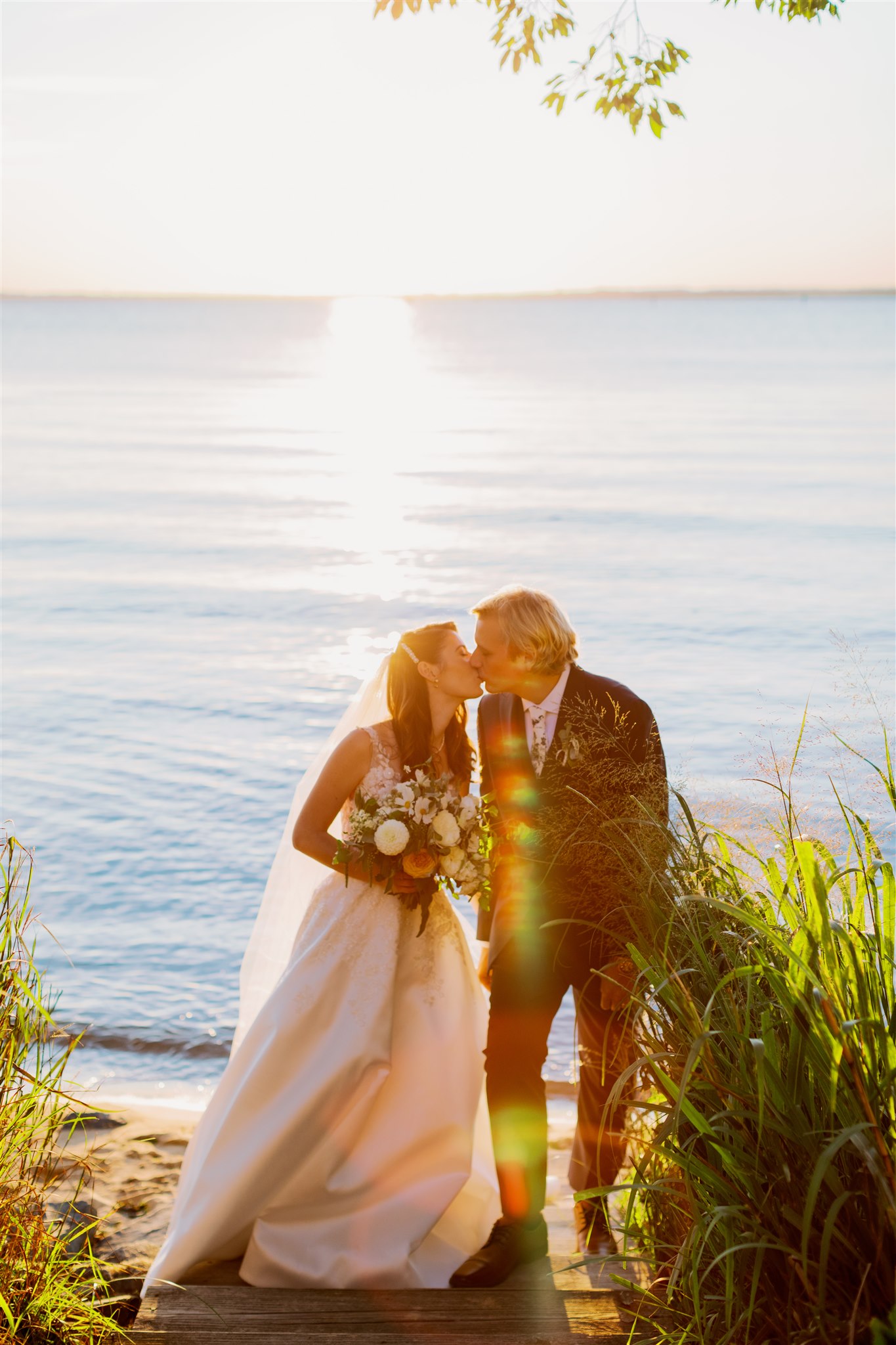 Bride and groom kiss lakeside during golden hour of their Intimate Waterfront Wedding at Chesapeake Bay Beach Club in Kent Island, MD. Image by Victoria Heer, Washington DC wedding photographer.