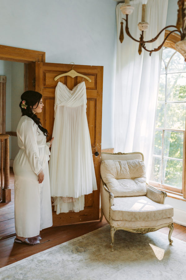 A robed bride looks at her wedding dress as she prepares to get ready at a Virginia mountain wedding venue. Image by Virginia wedding photographer Victoria Heer.