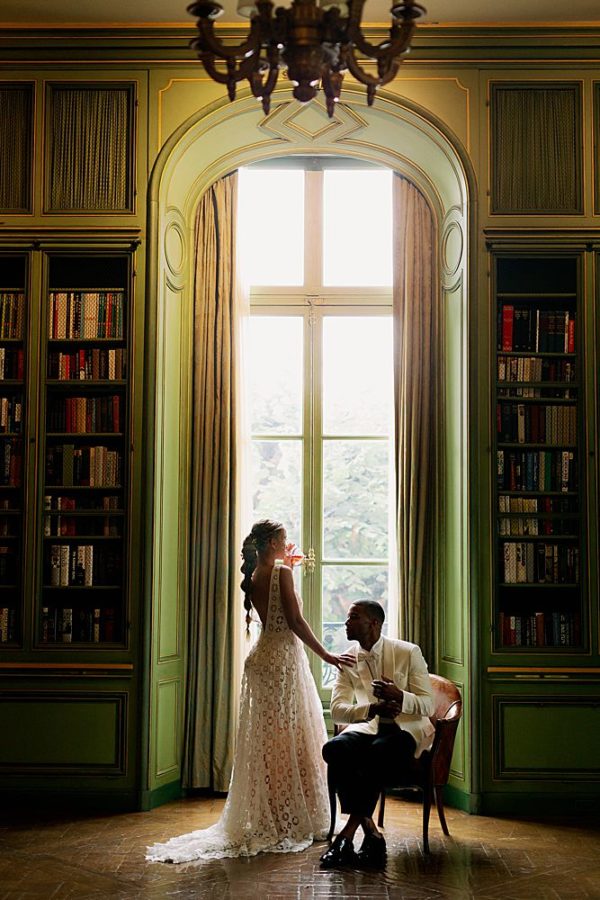 A bride and groom pose in front of the arched windows of